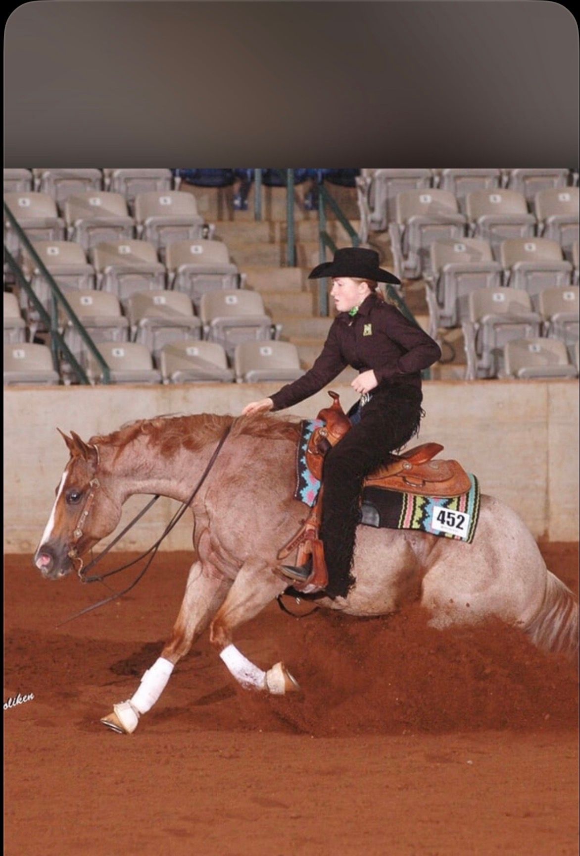 Cowgirl riding a horse in an indoor arena, leaning forward during a run.