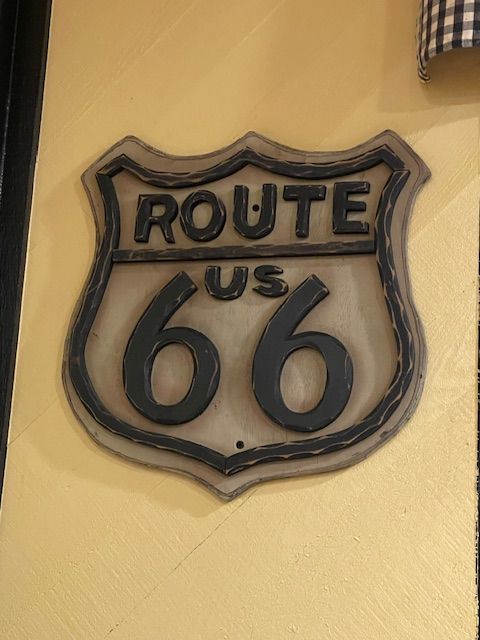 Route 66 sign in black and gray, mounted on a yellow wall.
