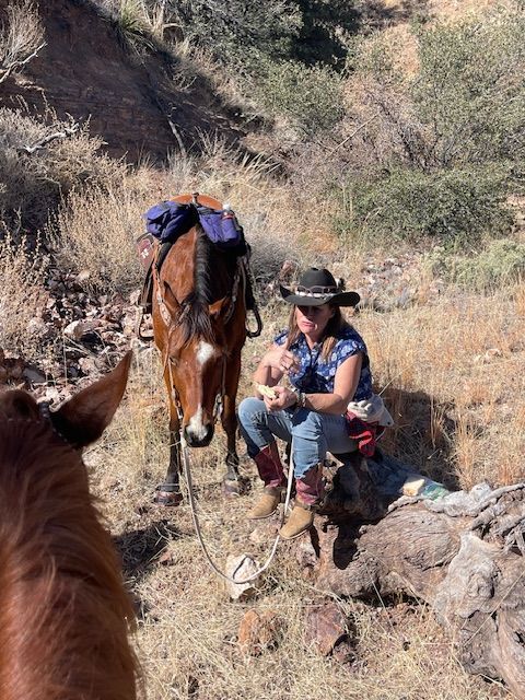 Woman in cowboy hat and horse resting on a hillside.
