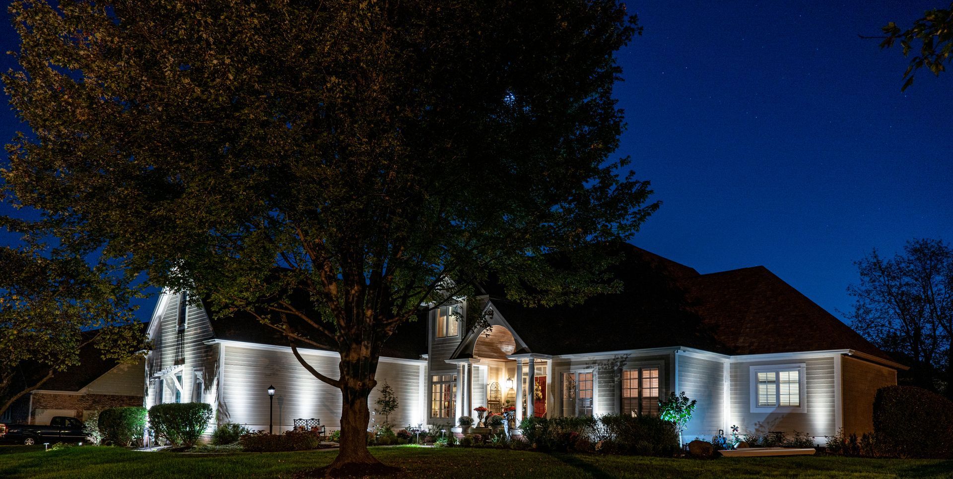 Lit up house at night with a tree in the foreground. Blue sky.