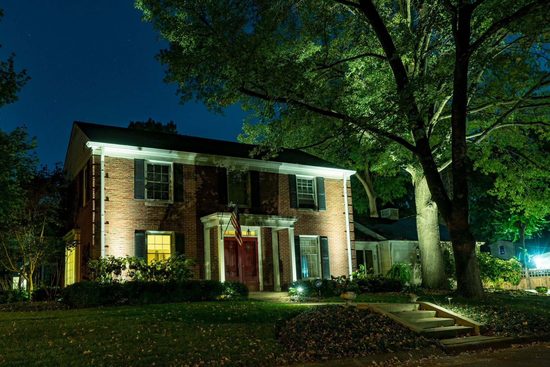 Lit brick house at night with illuminated tree and front steps.