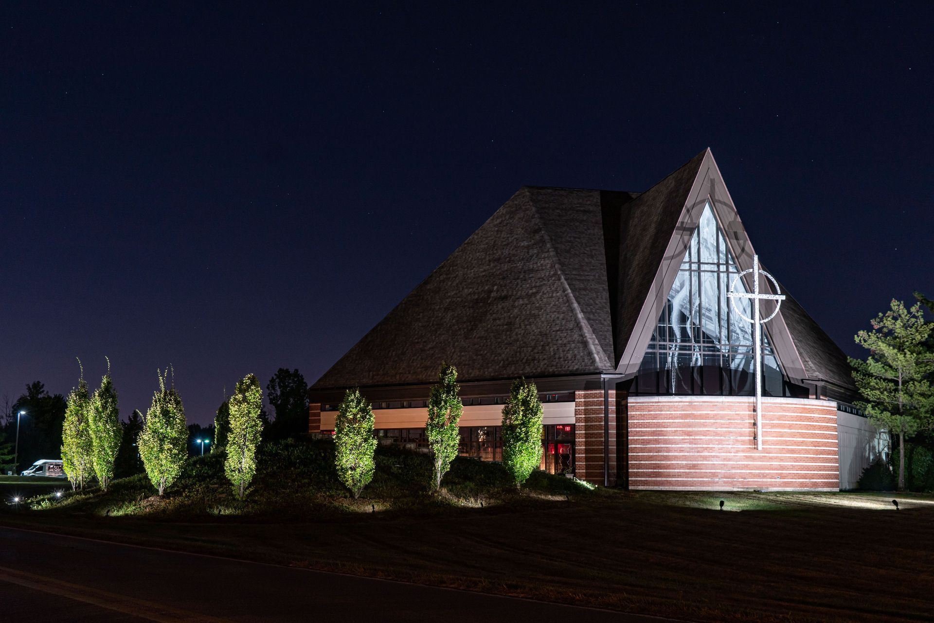 Church building at night with lit trees in front, dark sky.
