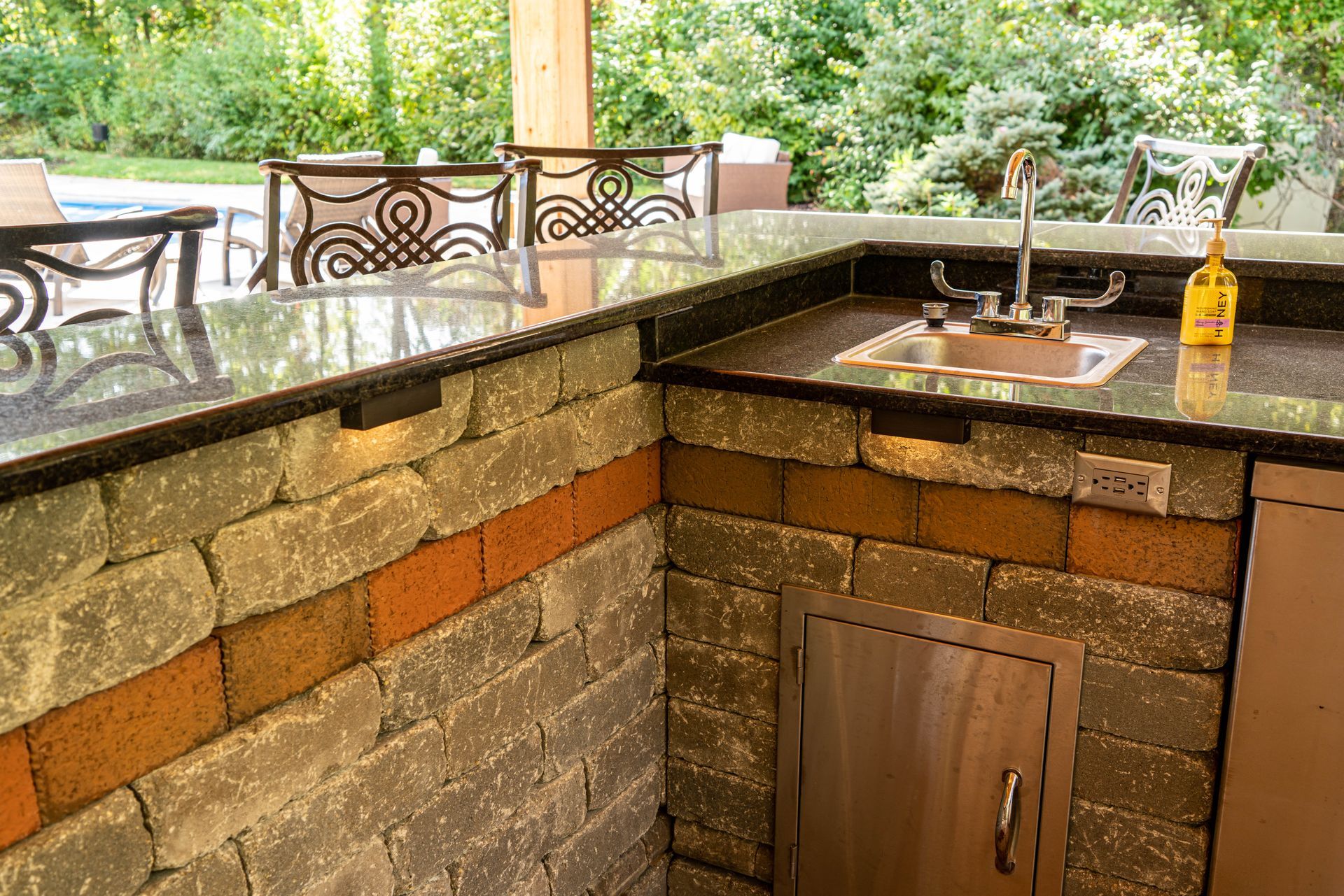 Outdoor kitchen with a brick facade, granite countertops, and a sink.