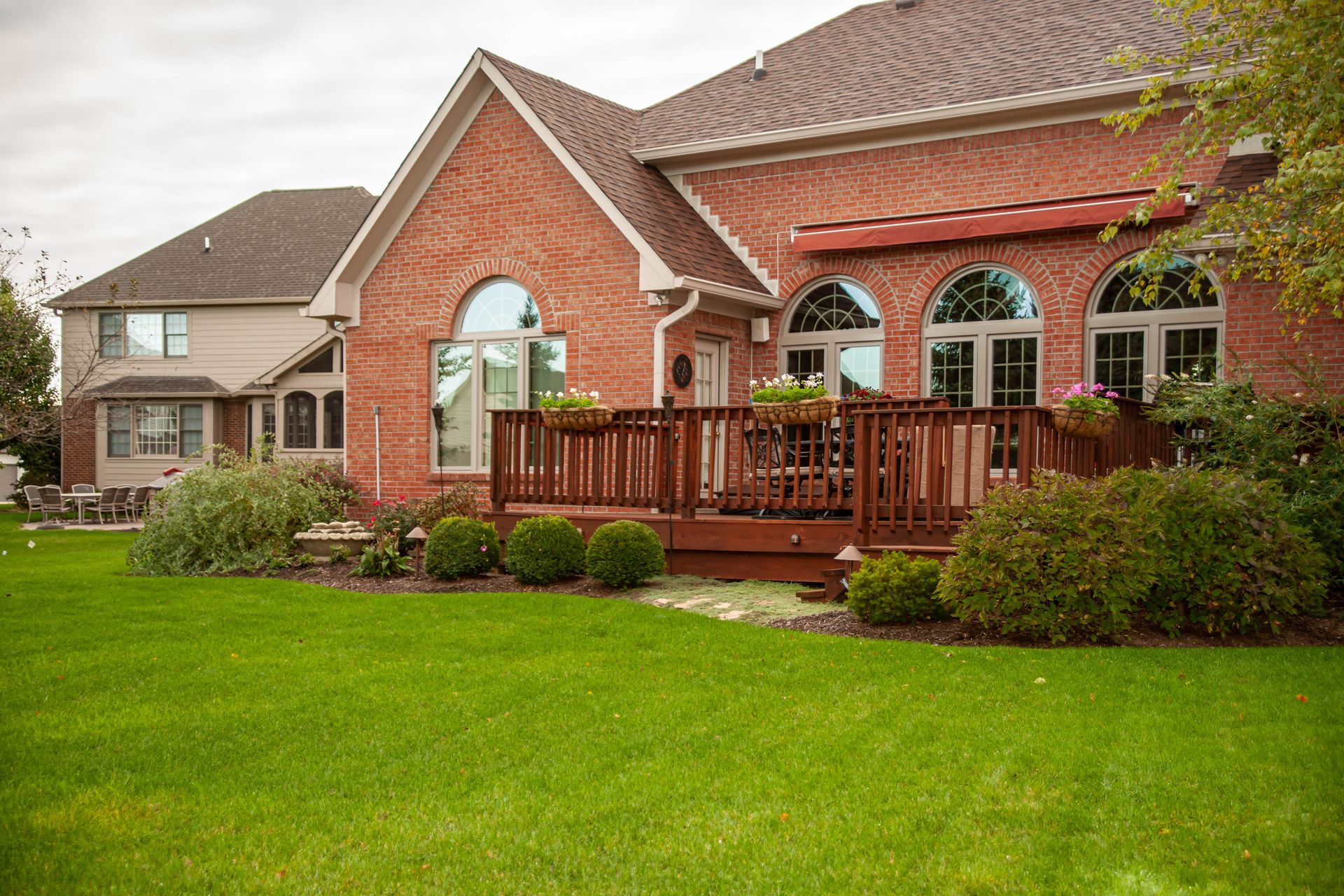 Red brick house with a wooden deck, green lawn, and shrubbery in the yard.