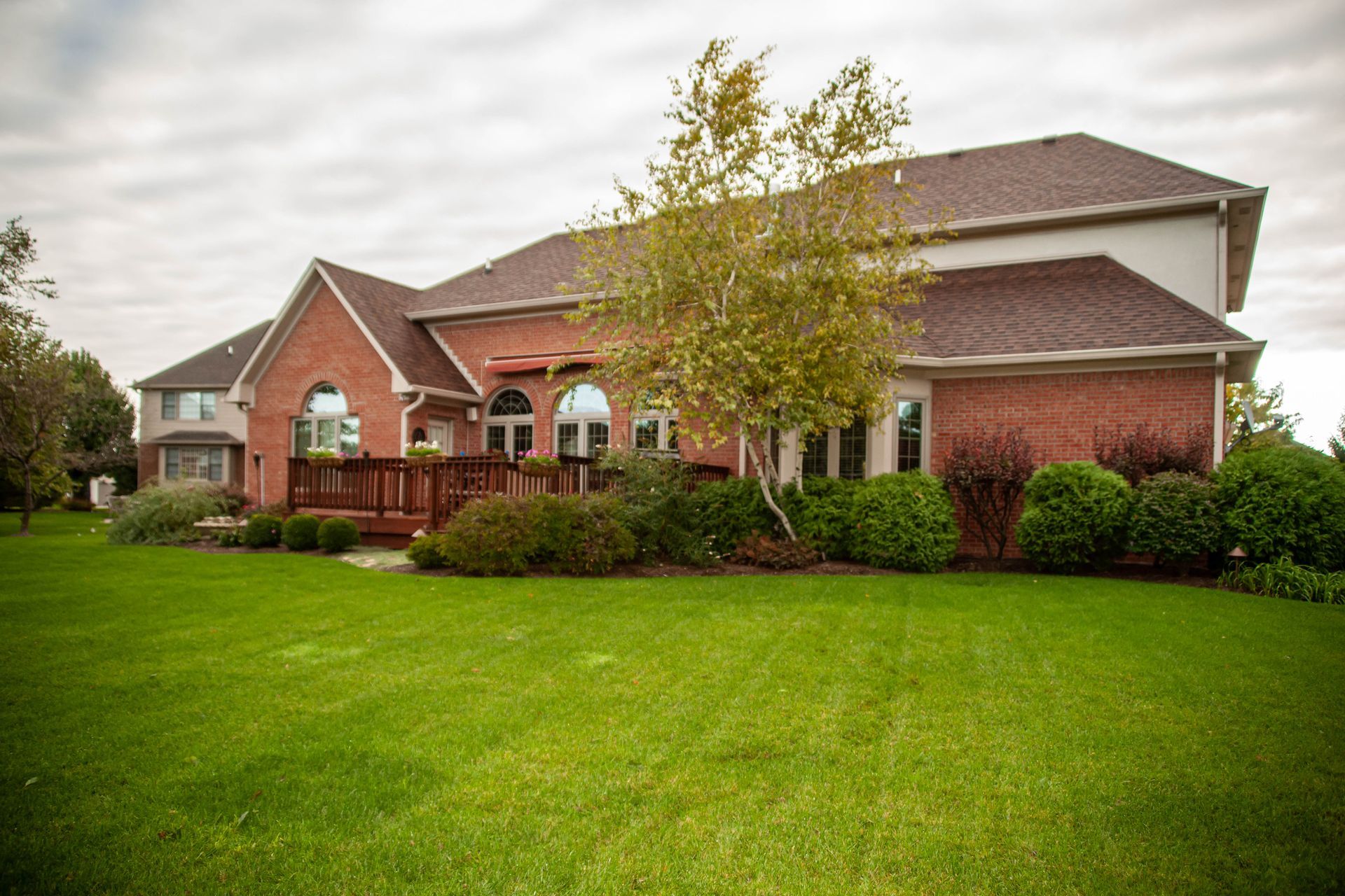 Brick house with green lawn and landscaping under a cloudy sky.