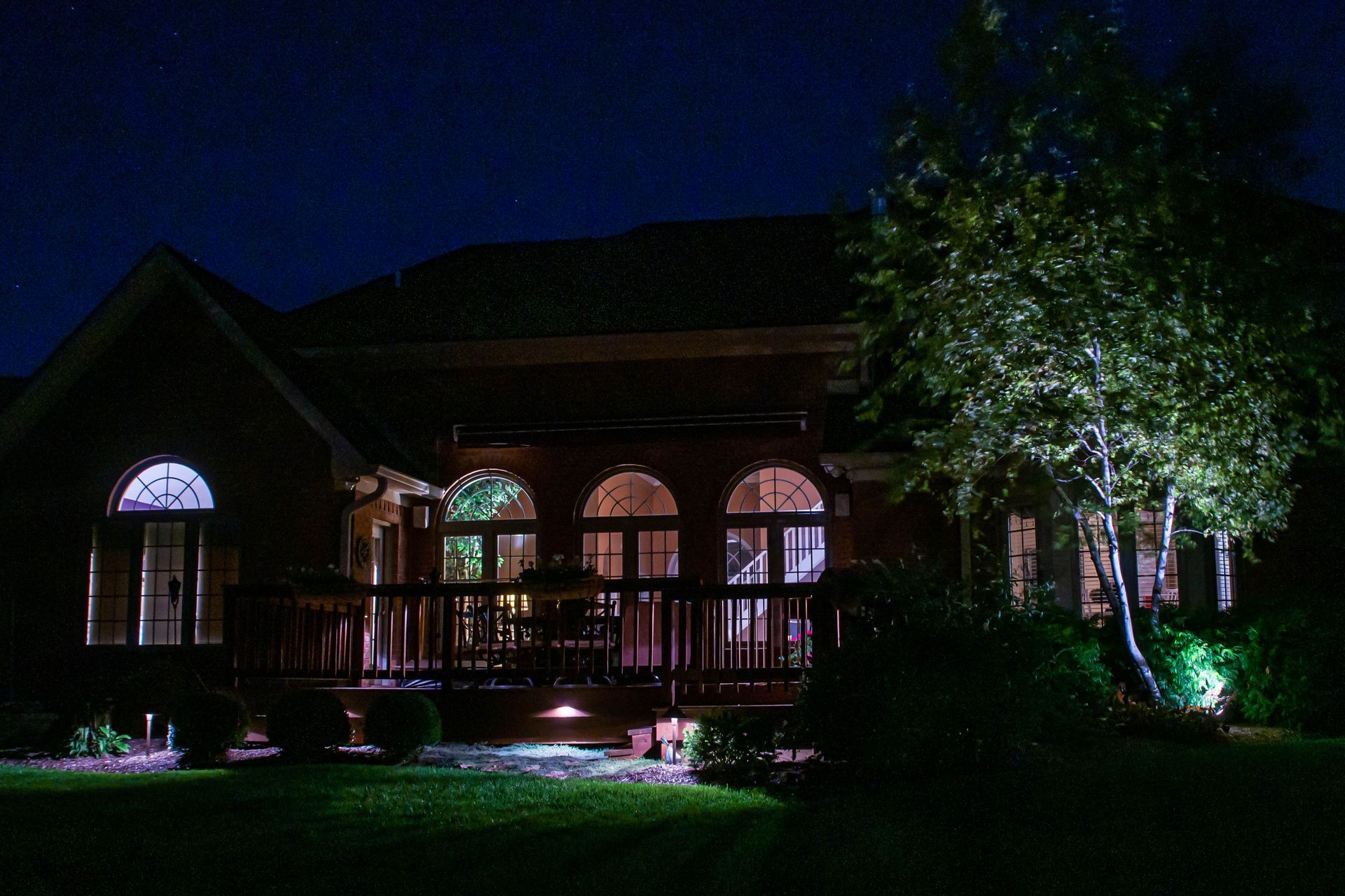 House lit up at night with backyard and illuminated tree.