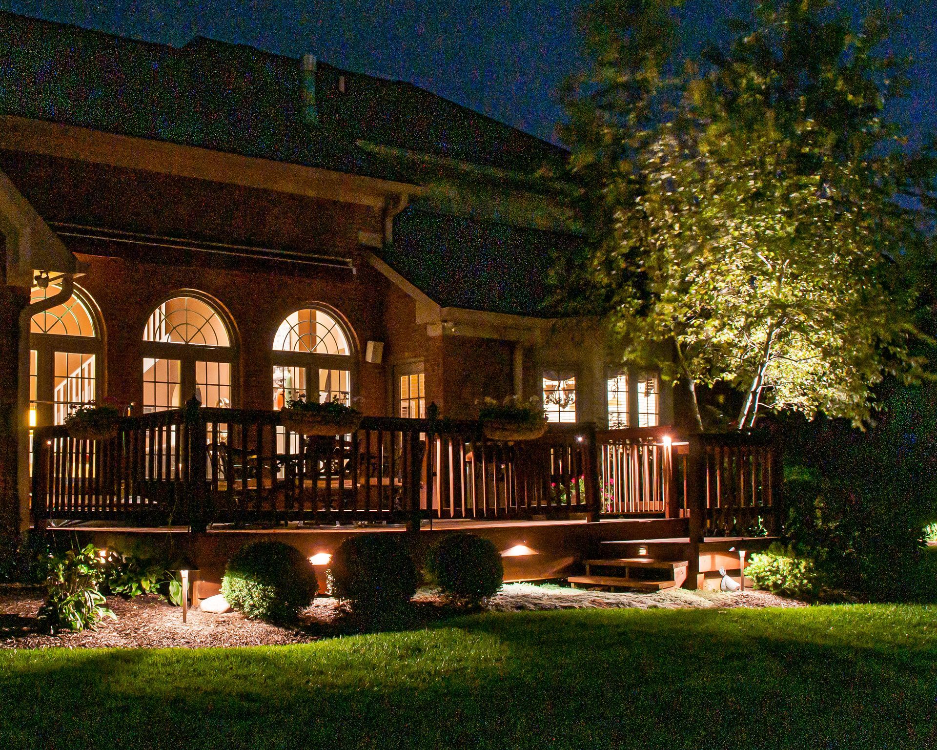 Nighttime view of a deck with built-in lighting, overlooking a lawn. The house is brick.