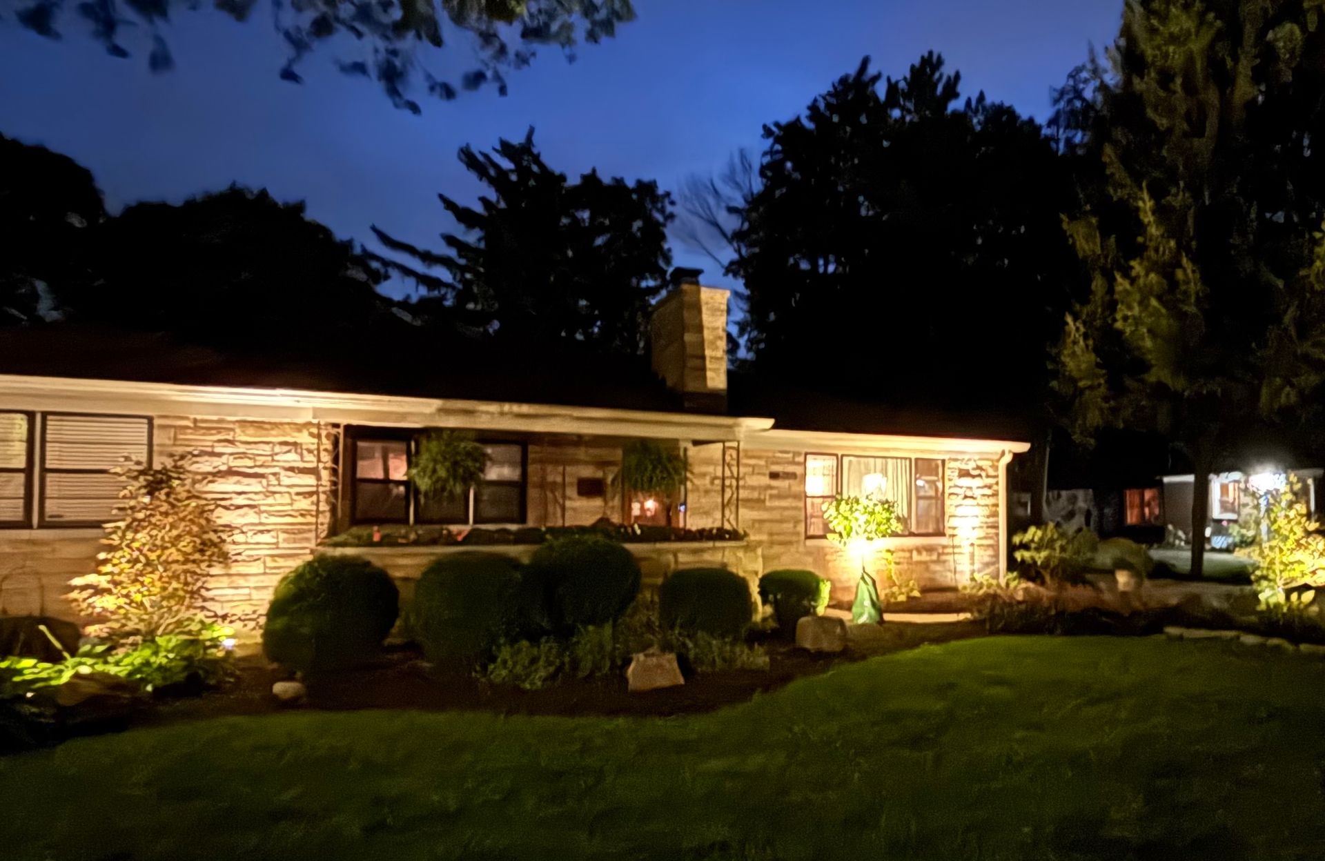 Stone house exterior lit at night, with landscaping and dark sky.