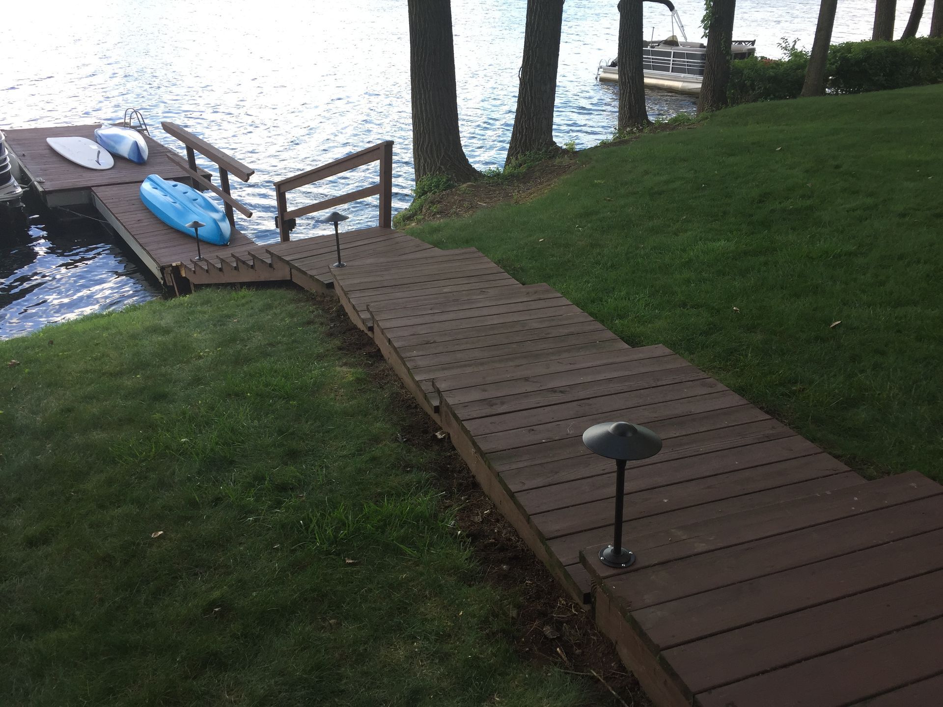 Wooden dock and stairs leading to a lake, with kayaks and landscape lighting.
