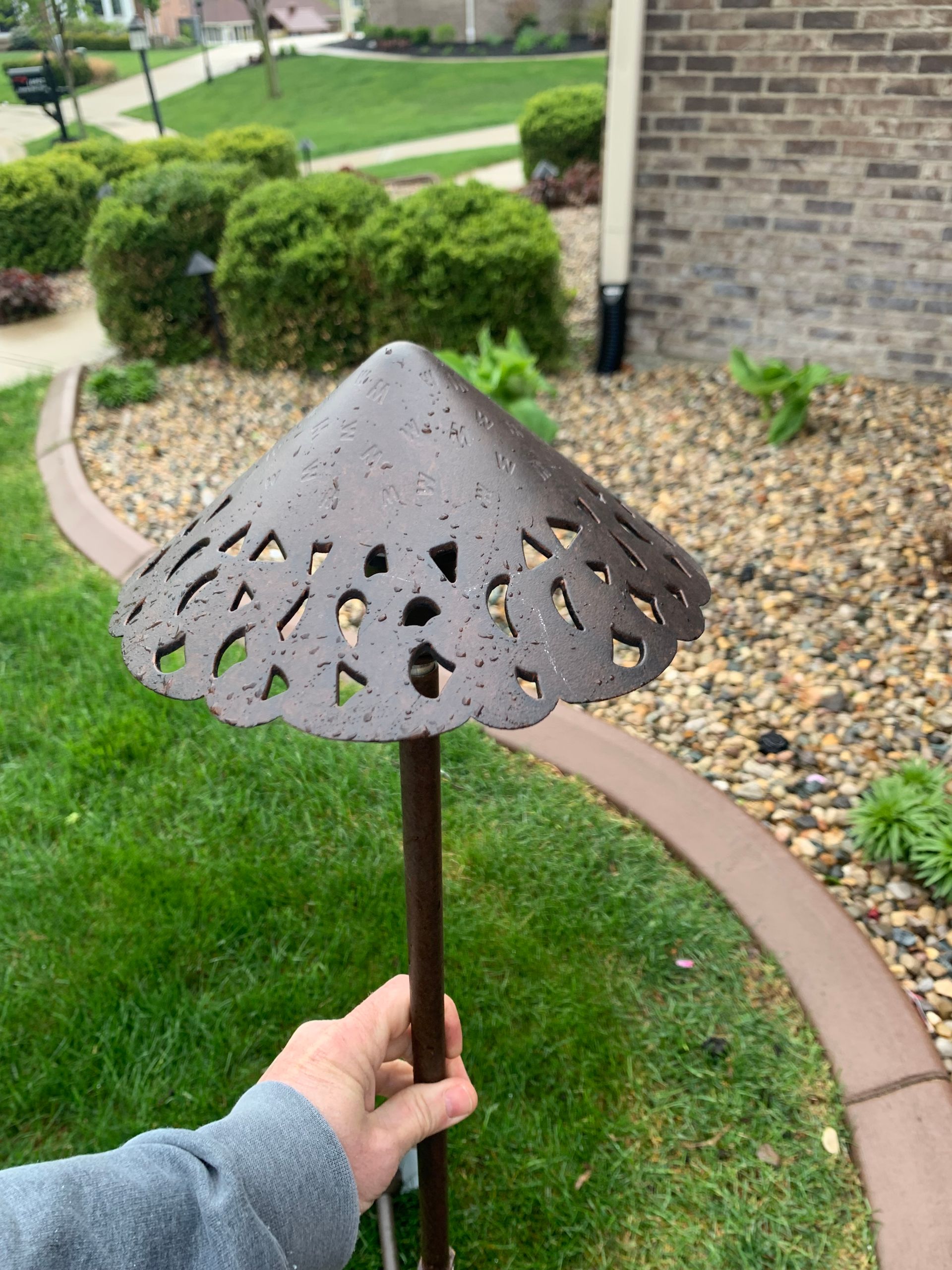 Person holding a brown metal landscape light with a decorative, scalloped shade, set in a yard.