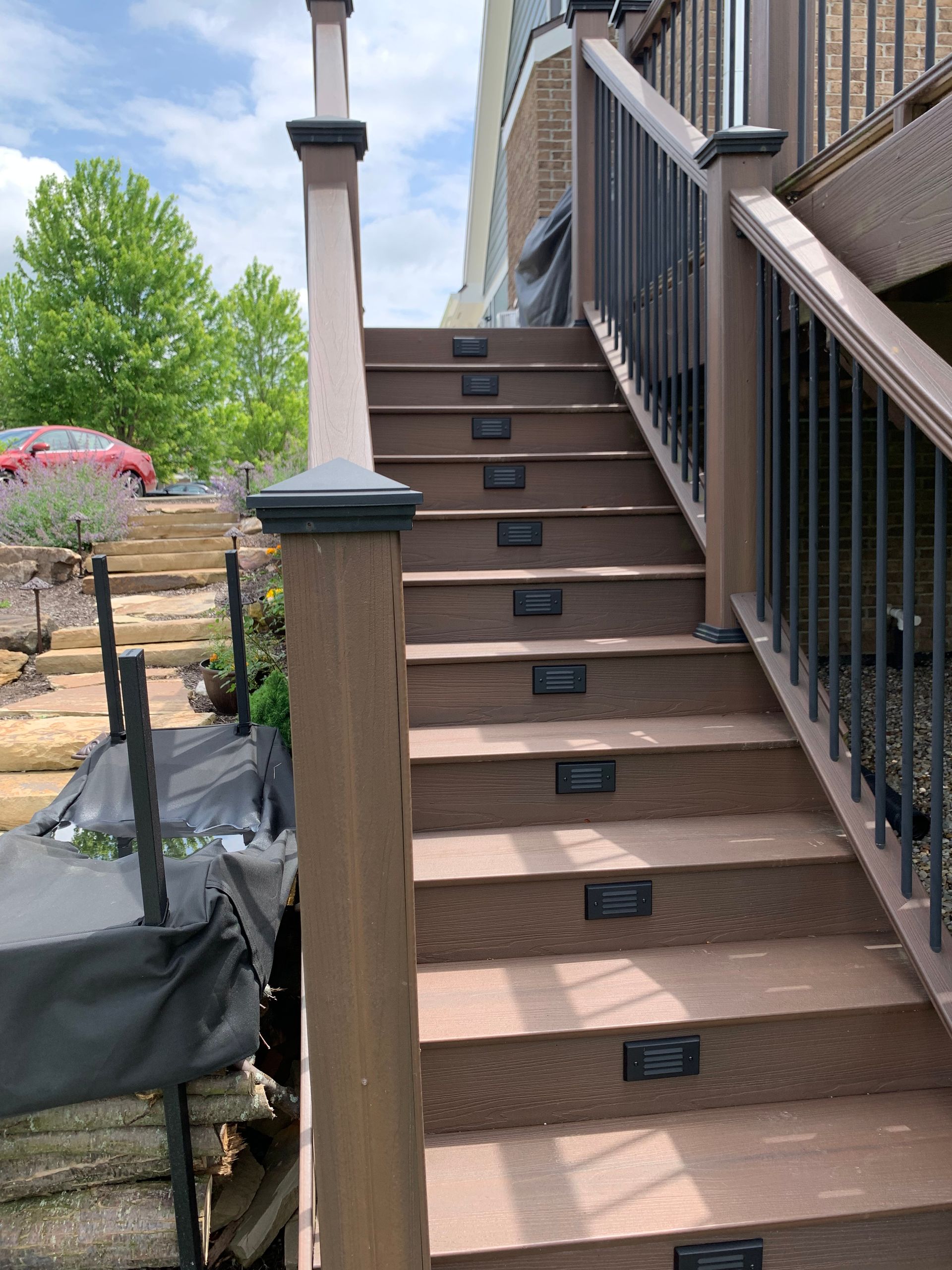 Wooden staircase with built-in lights, leading up to a deck with black railing and brown boards.