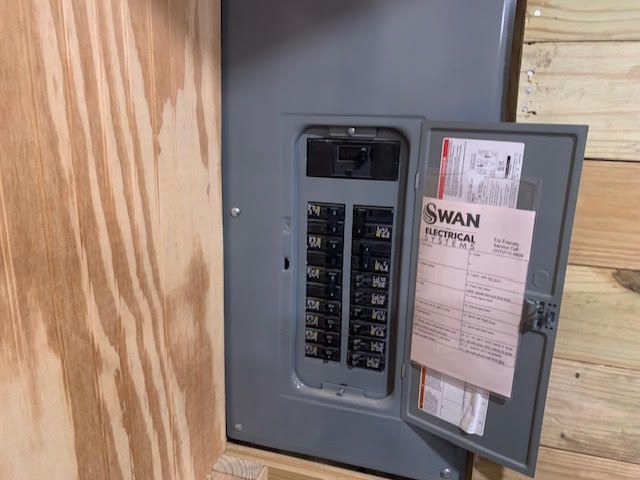 Electrical panel with door open, revealing circuit breakers and a document labeled