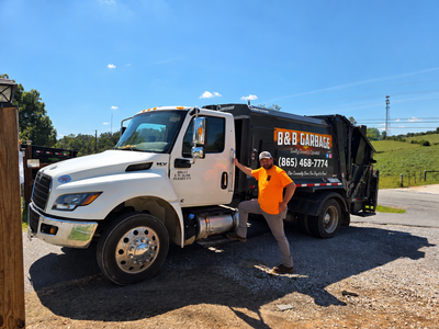 White and black dump truck with a person in an orange shirt standing by the cab on a sunny road