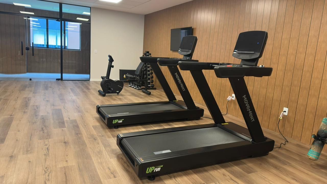 Academia com duas esteiras, bicicleta ergométrica e paredes revestidas de madeira.