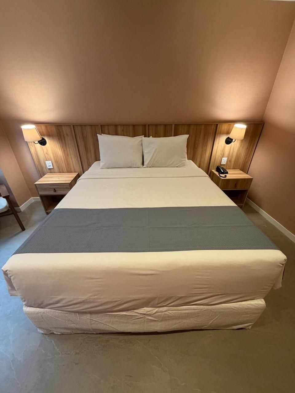 Quarto de hotel com cama, mesas de cabeceira, luminárias e uma parede cor de pêssego.