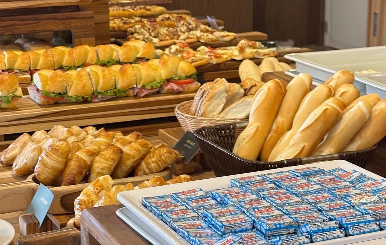 Buffet com variedade de pães, croissants, sanduíches e sachês individuais de manteiga.