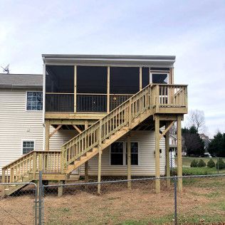 Two-story wooden deck with screened-in porch and stairs attached to a house with beige siding.