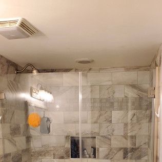 Shower with gray marble tile, glass door, showerhead, and a vent fan.