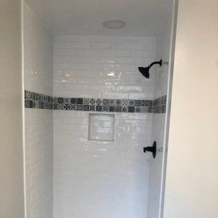 Tiled shower with black fixtures and decorative tile border. White and dark blue colors.