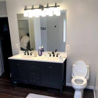Bathroom with dark blue vanity, double sinks, large mirror, toilet, and overhead lighting.