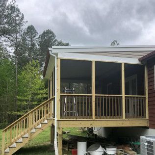 Wooden screened porch with stairs attached to a house with a cloudy sky backdrop.
