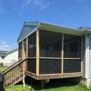Screened porch attached to a house with wooden stairs and blue siding, against a sunny blue sky.