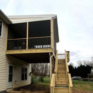 Exterior view of a raised wooden deck with stairs. The deck is attached to a house with a screened porch on top.