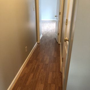 Narrow hallway with wood-look flooring and light grey walls, doors on the right.