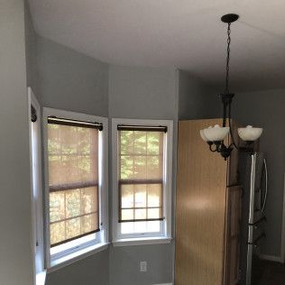 A kitchen with two windows and beige blinds, a chandelier, and a refrigerator.