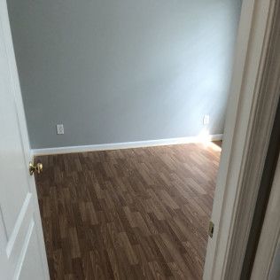 Empty room with wood-look floor, gray walls, and white door frame.