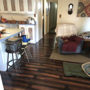 Interior view: kitchen with dark wood floors, a barstool, and a living area with an armchair.