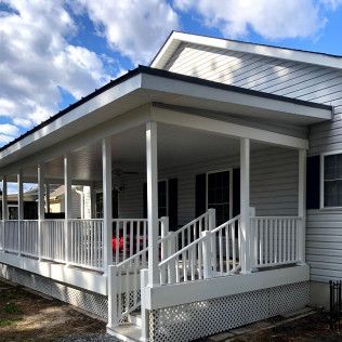 White porch with railings, stairs, and columns; attached to a gray house with a black roof.