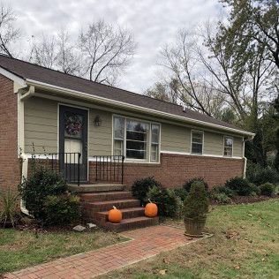 Tan house with brick facade, steps, and pumpkins on display.