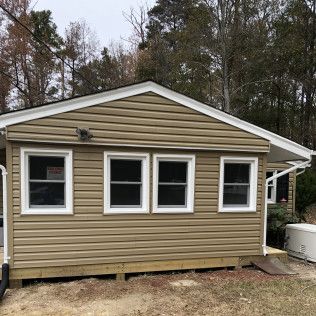 Tan-sided small house with three windows, white trim, and a small ramp.