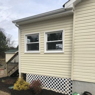 Exterior of a house with two windows, light yellow siding, and lattice under the windows.