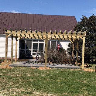 Wooden pergola over a concrete patio outside a white building with a brown roof and American flag.