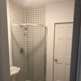 Small bathroom with penny tile shower, glass door, white door on right.