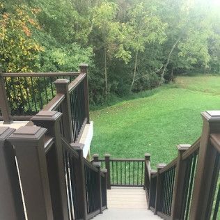 Wooden deck with stairs leading to a grassy yard surrounded by trees.
