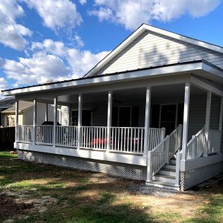 White screened porch attached to a light-colored house with a dark roof against a blue sky.
