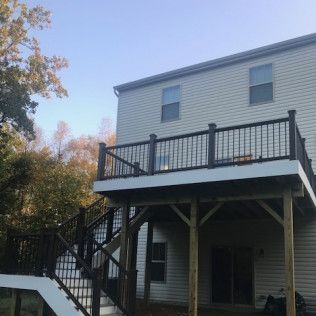 Two-story house with a wooden deck and stairs. The deck has black railings.  Clear blue sky.