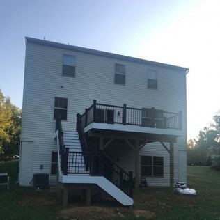 Two-story house with a white exterior, a deck, and a set of stairs. Black railings and supports.