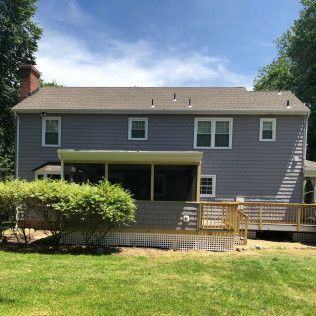 Back of a two-story gray house with a deck, screened porch, and green lawn on a sunny day.