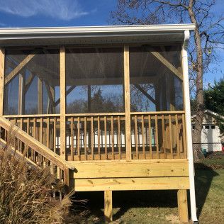 Wooden screened-in porch with railing and stairs, attached to a house with white gutters.