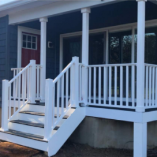 White porch with steps, columns, and railing, leading to a blue house with a red door.