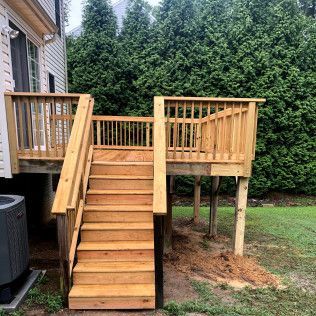 Wooden deck with stairs leading down into a grassy yard, with evergreen trees in the background.