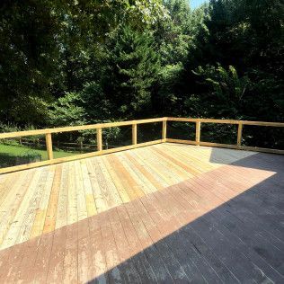 Wooden deck with light-colored boards and railing overlooking green trees. Sunny outdoor setting.