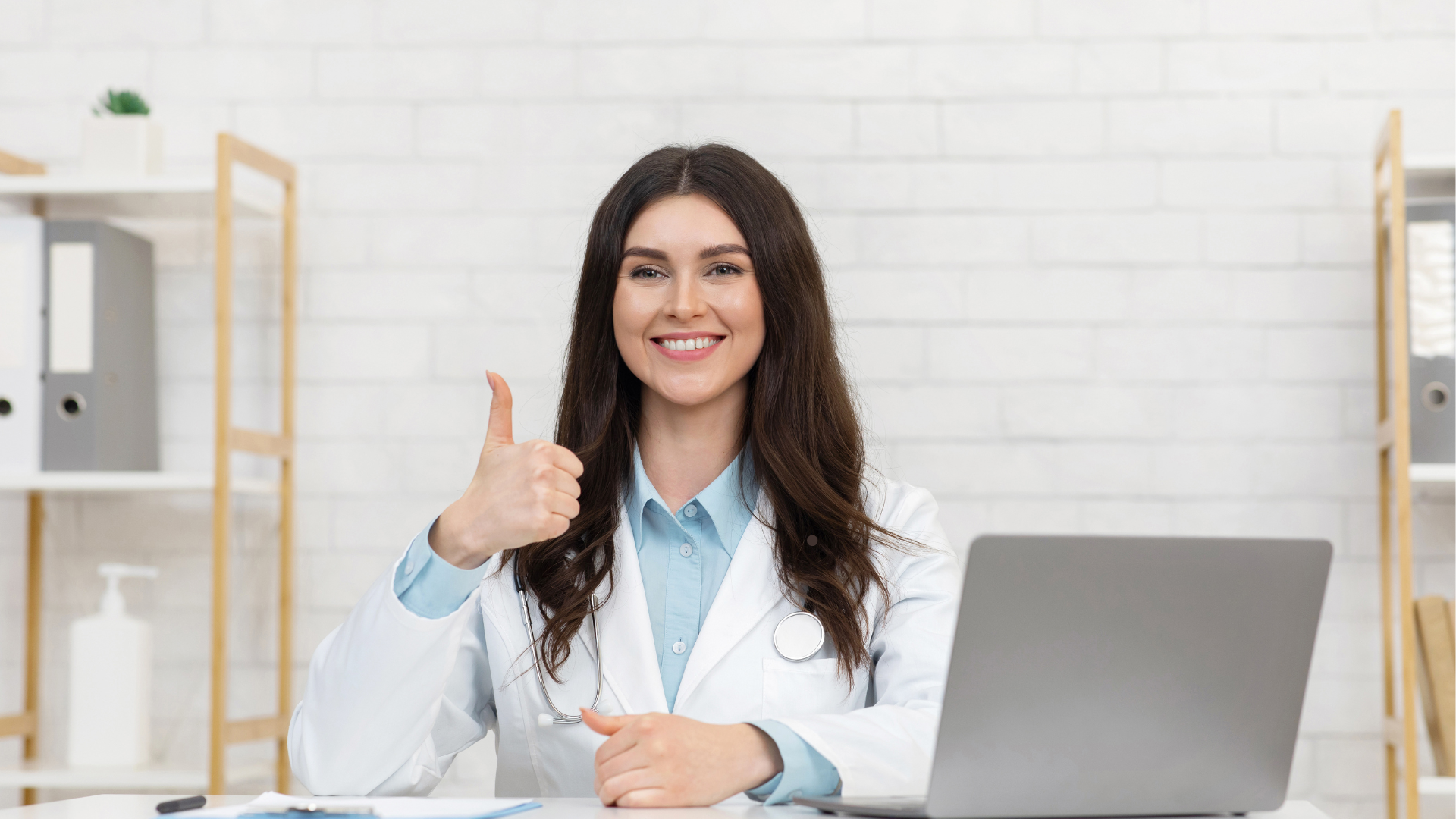 Female psychiatrist smiling while giving a thumbs-up during a telehealth consultation, seated at a desk with a laptop, representing professional ADHD care and online treatment support.