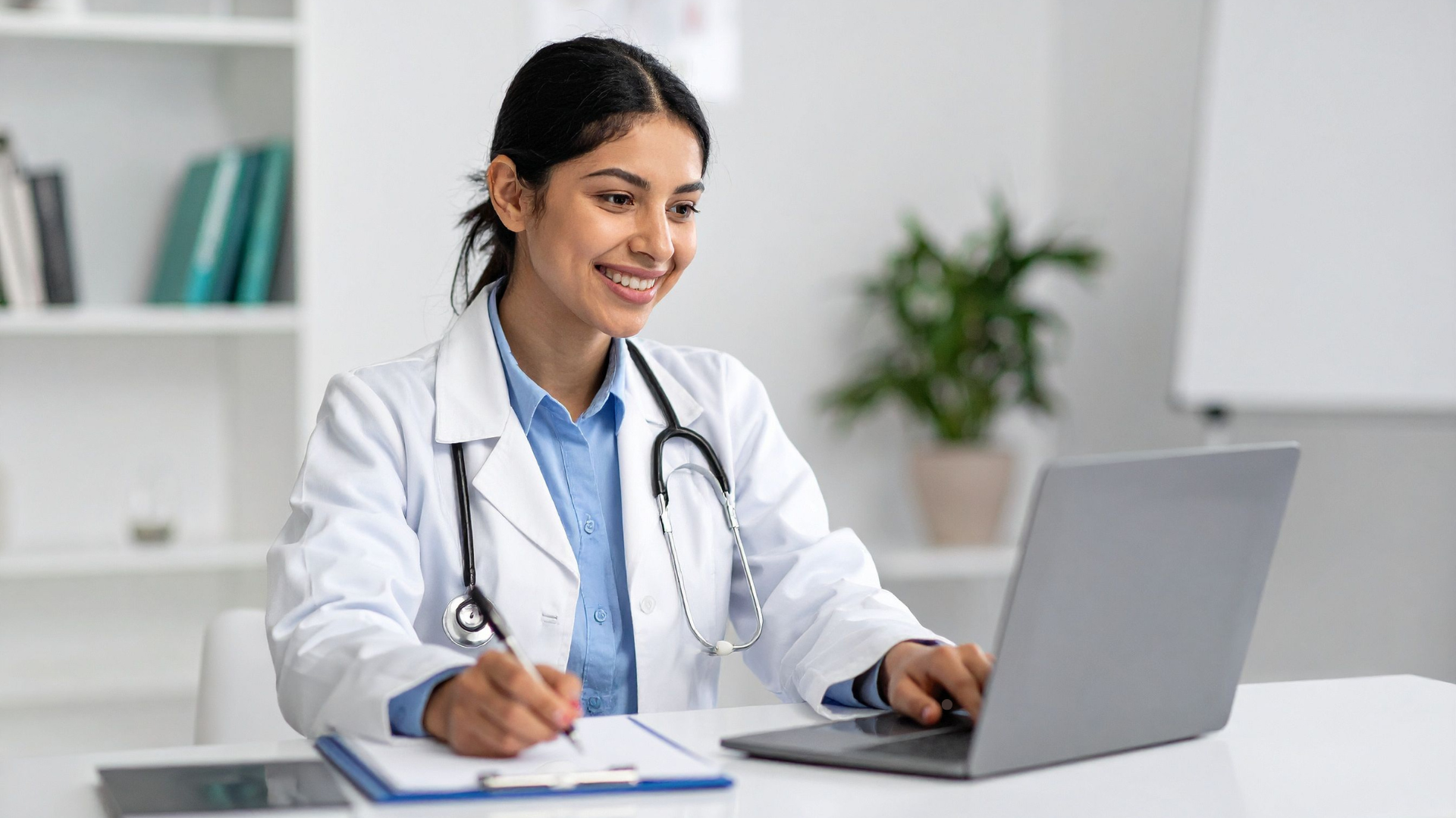 Female psychiatrist smiling while working on a laptop during a virtual consultation, representing online psychiatric medication management and telepsychiatry services.