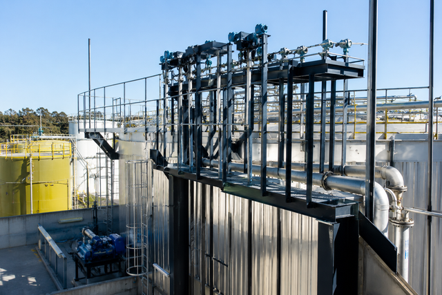 Equipos industriales en azoteas con tuberías metálicas, tanques y barandillas a plena luz del día.