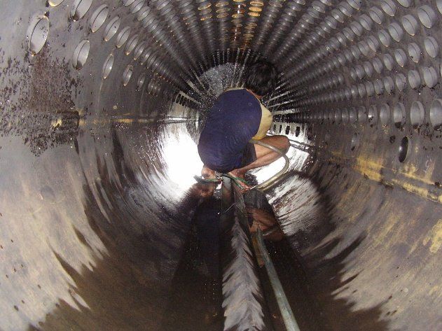 Un trabajador se encuentra dentro de un gran tubo o túnel de metal corrugado, con una luz brillante en el extremo opuesto.